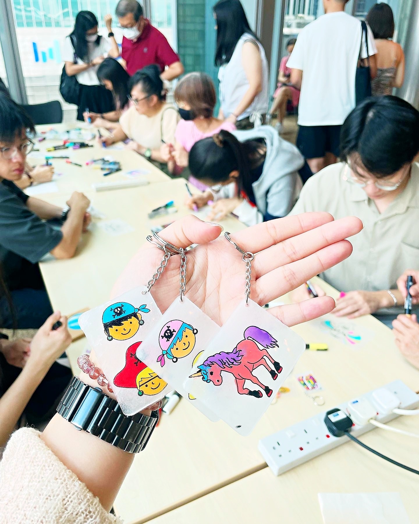 Colourful shrink art keychains held above a workshop table